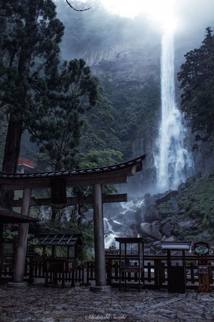 a large waterfall in the middle of a forest next to a wooden structure and trees