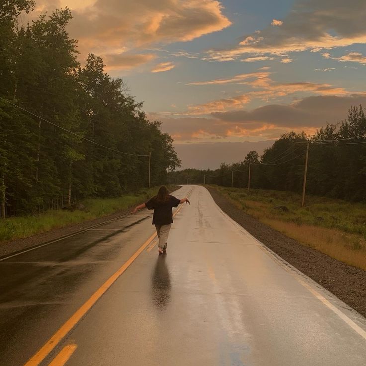 a person walking down the road in the rain with an umbrella over their head as the sun sets