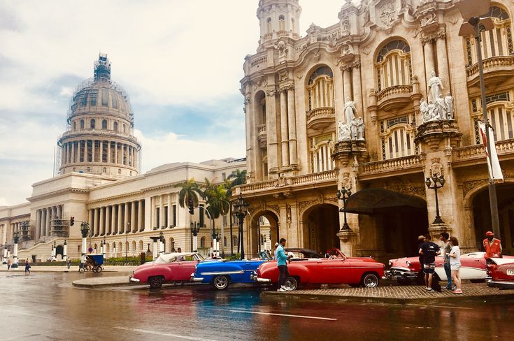 classic cars parked in front of an old building on a rainy day with people walking by