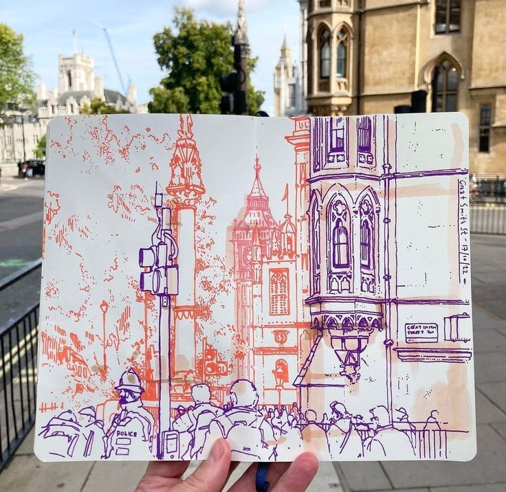 a hand holding up a piece of paper with drawings on it in front of a building