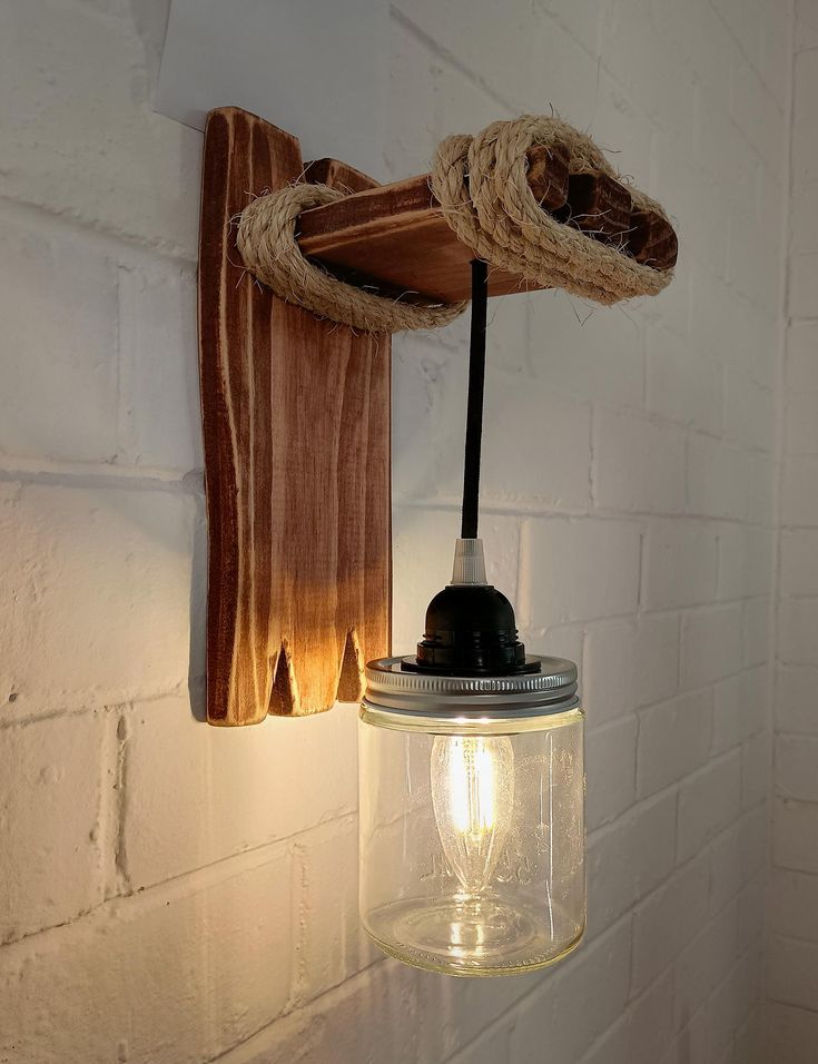 a mason jar light hanging from a rope on a wall next to a brick wall