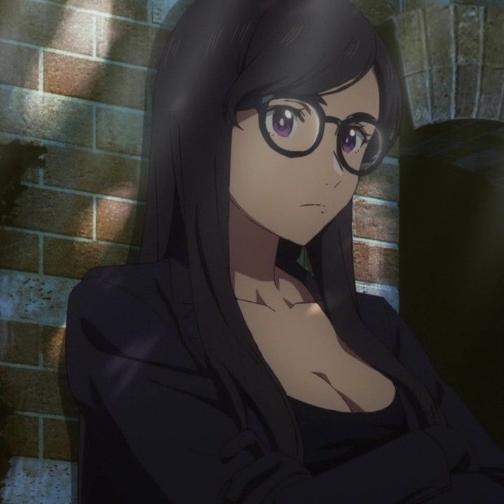 a woman with glasses standing in front of a brick wall and looking at the camera