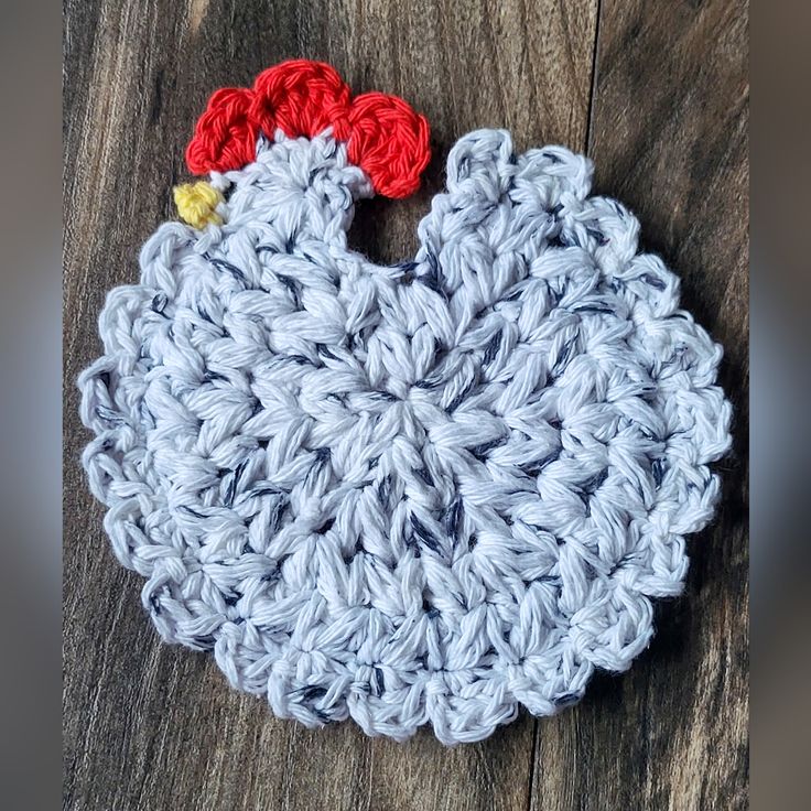 a crocheted chicken ornament sitting on top of a wooden floor next to a piece of wood