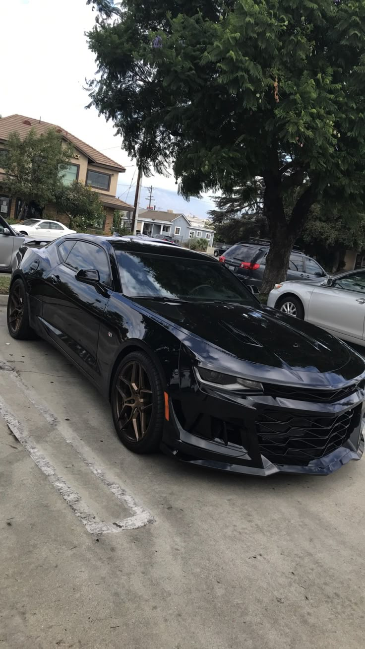 a black chevrolet camaro is parked in a parking lot next to some trees and cars