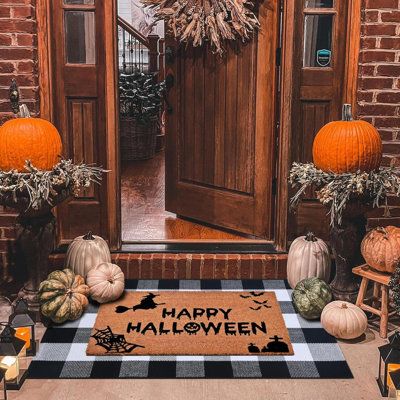 a welcome mat with happy halloween written on it in front of a brick door surrounded by pumpkins and gourds