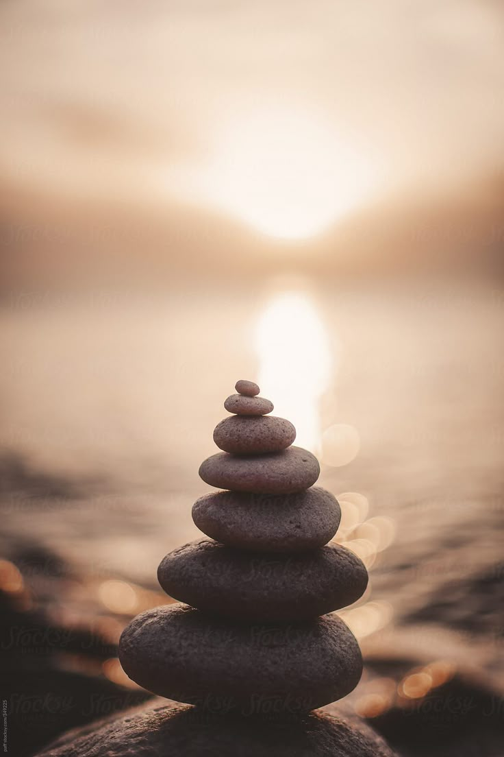 rocks stacked on top of each other in front of the ocean with the sun setting behind them