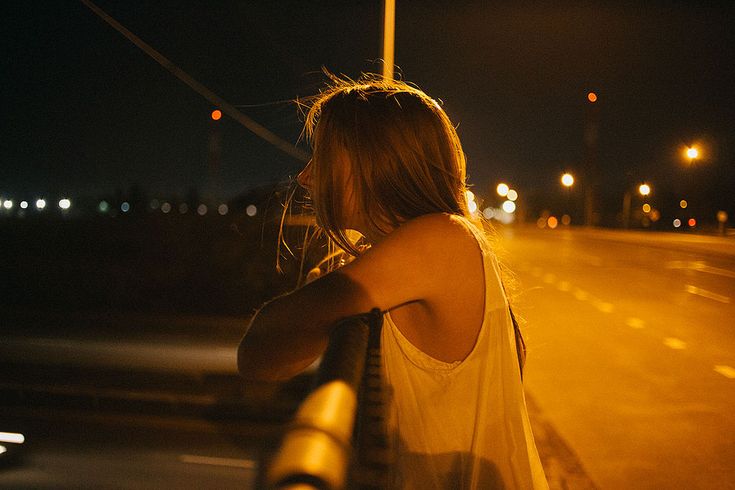 a woman standing on the side of a road at night with her arms behind her head