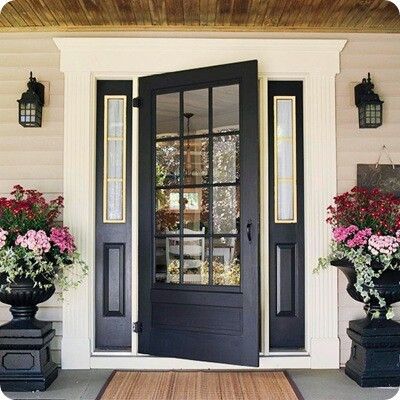 the front door is painted black and has flowers in large urns on either side