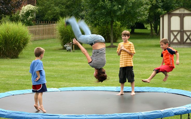 three children are playing on a trampoline in the yard while one boy is upside down