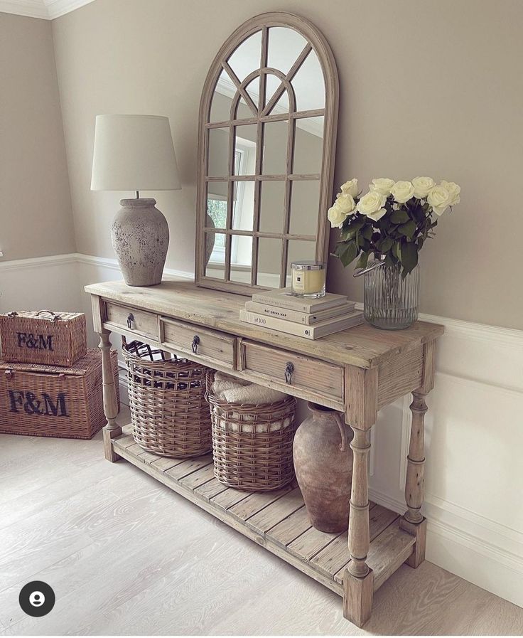 a wooden table with baskets and vases on it next to a wall mounted mirror