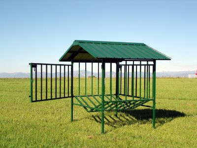 a green metal structure in the middle of a grassy field with a red truck behind it