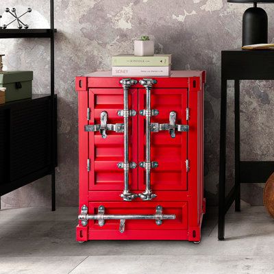 a red cabinet sitting on top of a floor next to a table with a lamp