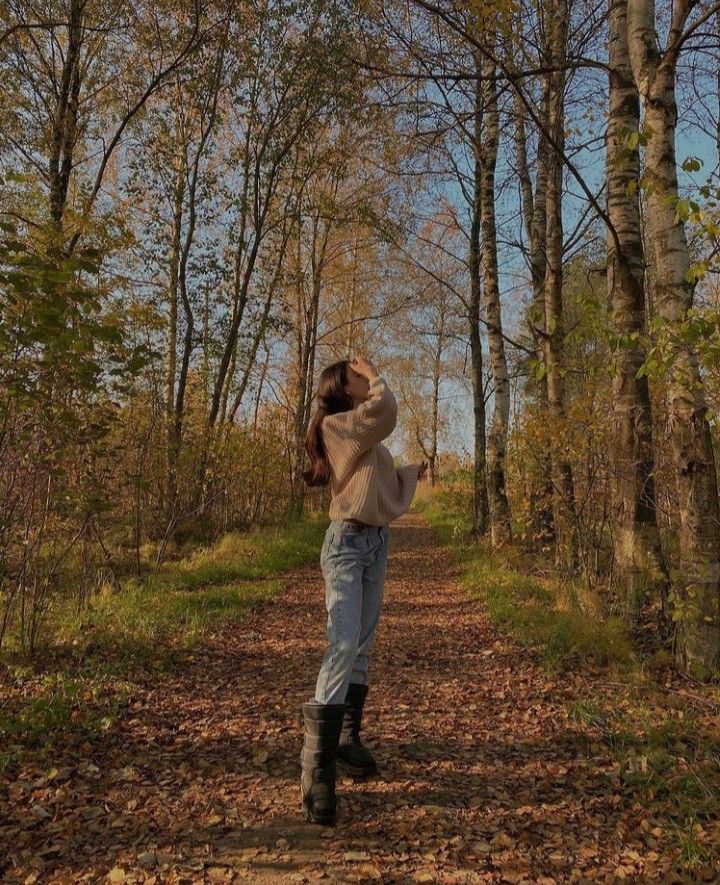 a woman standing in the middle of a leaf covered forest with her hands behind her head