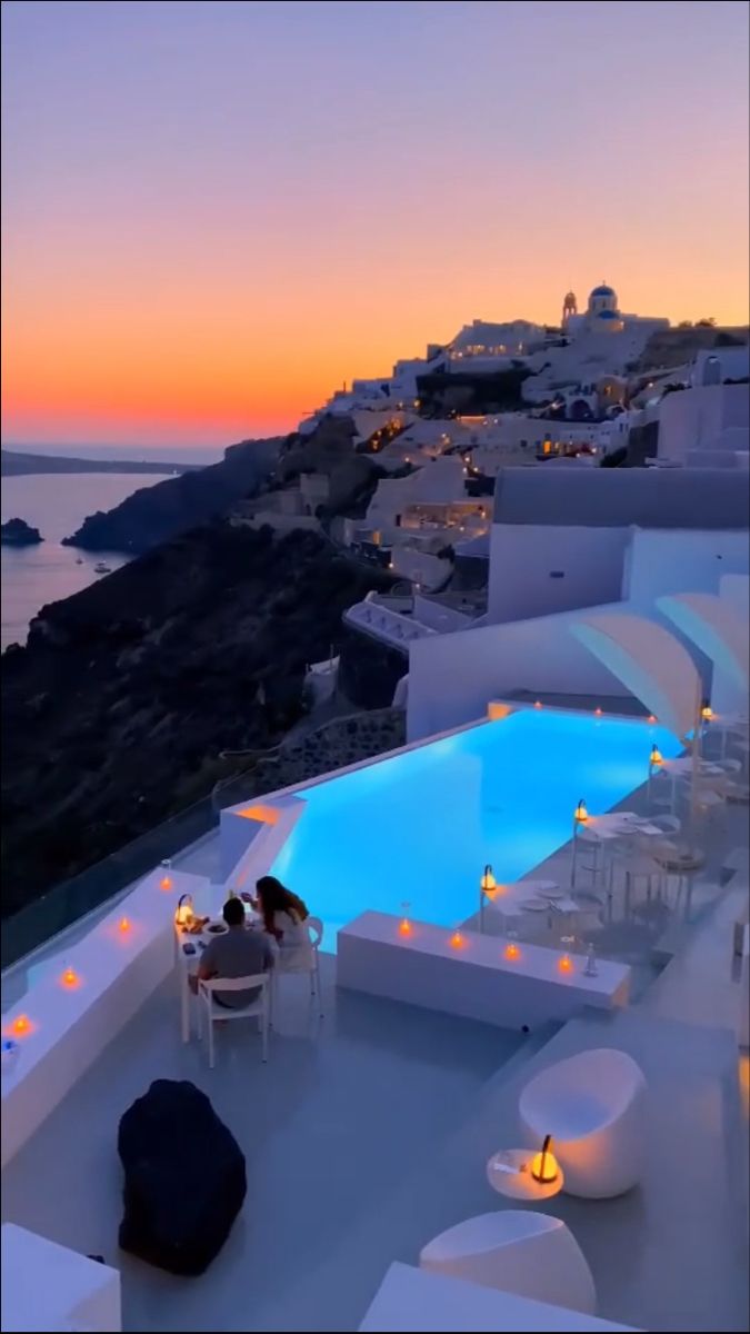 an outdoor dining area overlooking the ocean at dusk with candles lit on tables and chairs