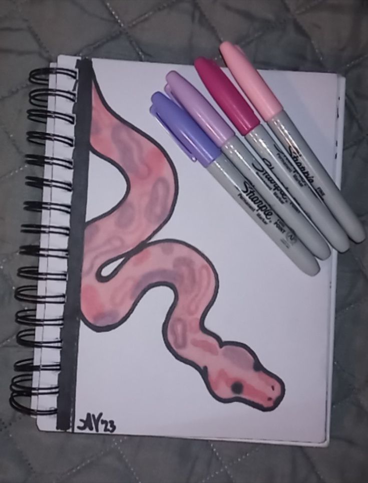 three pens are sitting on top of a spiral notebook with an image of a worm