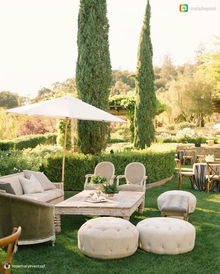 an outdoor seating area with chairs, tables and umbrellas on the grass in front of some trees