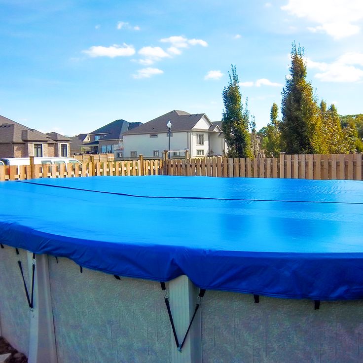 a blue tarp covering an above ground swimming pool in a residential area with houses behind it