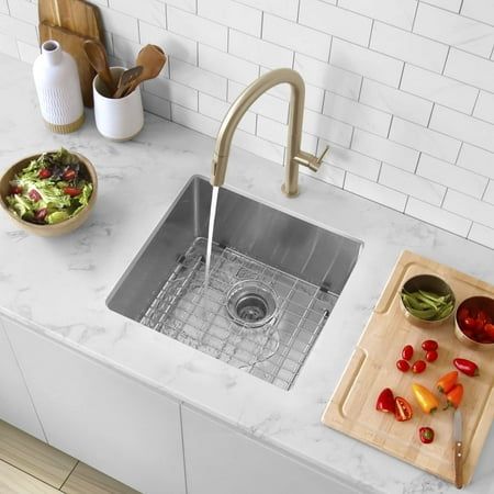 a kitchen sink with a cutting board on the counter next to it and bowls of vegetables