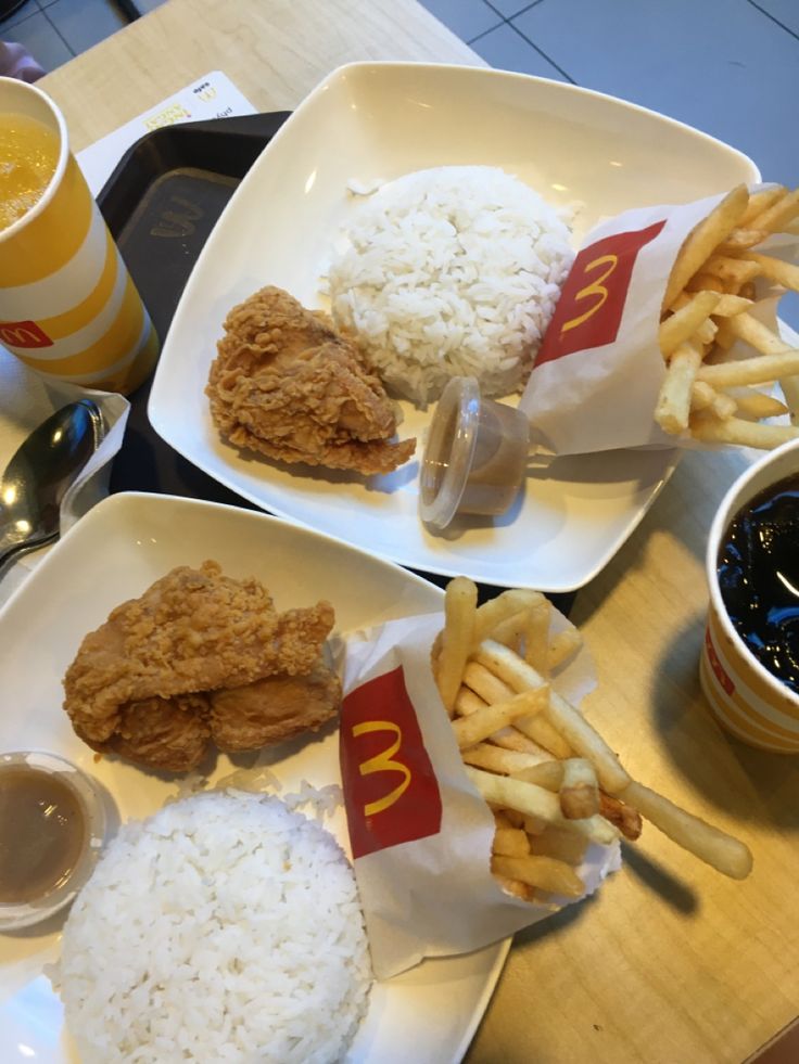 two white plates topped with chicken, rice and fries