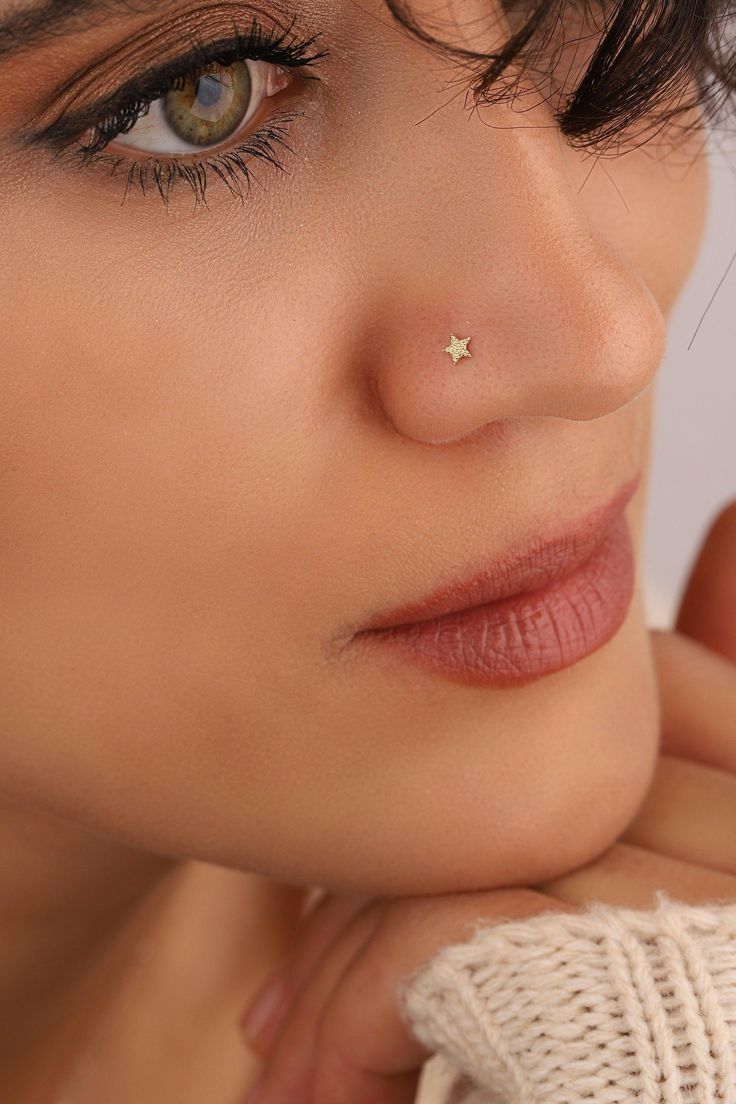 a close up of a person with a nose piercing on their left side and her right hand under her chin