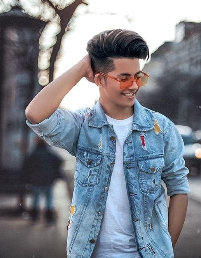 a young man in white shirt and blue jean jacket walking down the street with his hand on his head