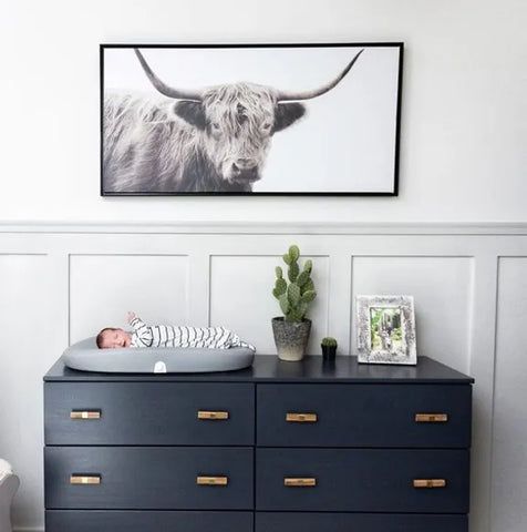 a baby in a crib next to a cow print on the wall above it