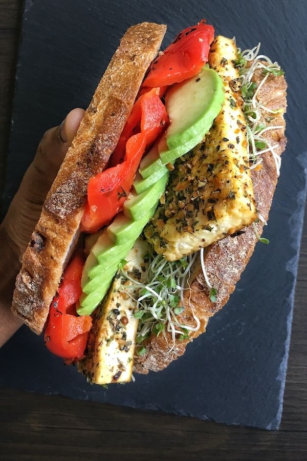 a hand holding a sandwich with meat, tomatoes and lettuce