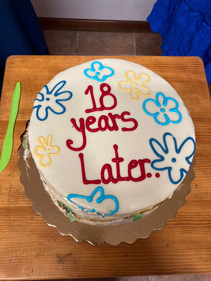 a decorated birthday cake sitting on top of a wooden table next to a knife and fork