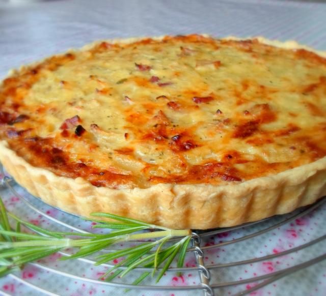 a quiche sitting on top of a wire rack next to a sprig of rosemary