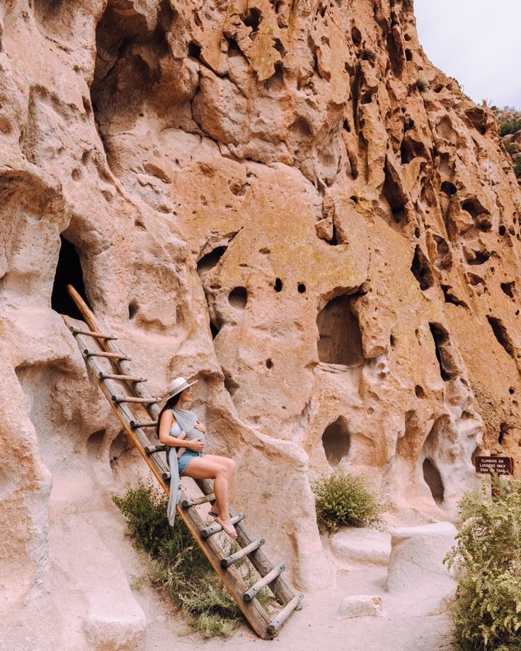 a woman sitting on top of a wooden ladder next to a rock formation with holes in it