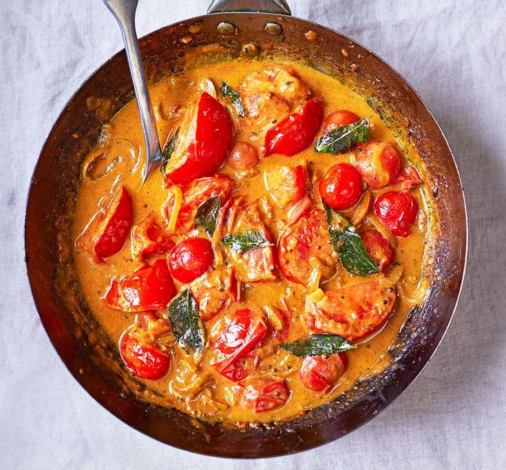 a skillet filled with chicken and tomatoes on top of a white cloth covered table