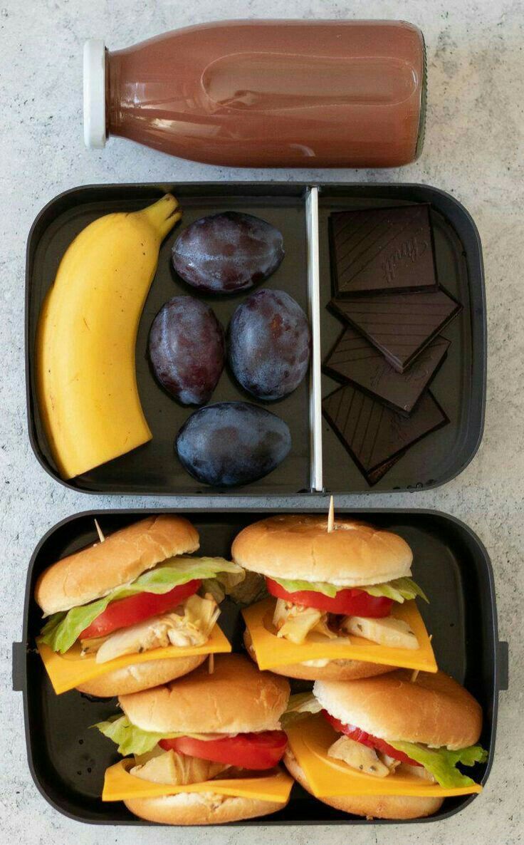 two trays filled with sandwiches, fruit and chocolate