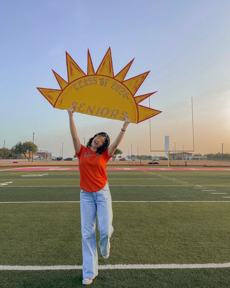 a woman holding up a sign on top of a field with her hands in the air