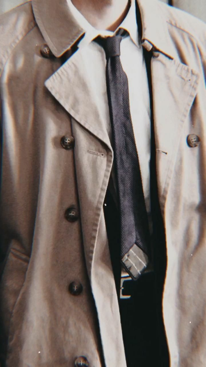 a man wearing a trench coat with a blue tie and white shirt in the background