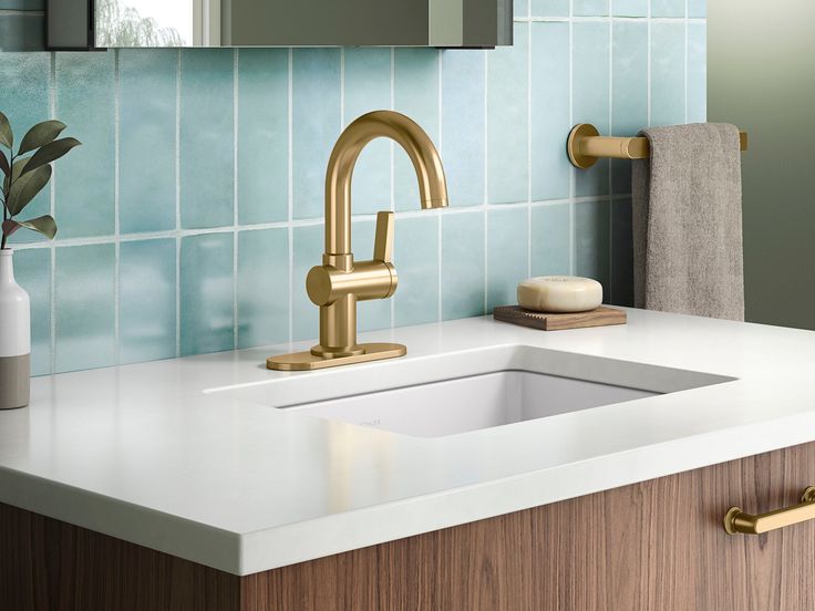 a bathroom sink with a gold faucet next to a mirror and towel dispenser