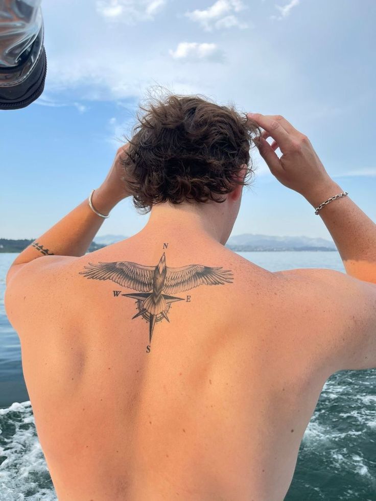 a man with a tattoo on his back looking out at the ocean from a boat