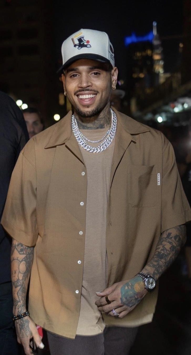 a man with tattoos and a baseball cap smiles for the camera while standing in front of a crowd