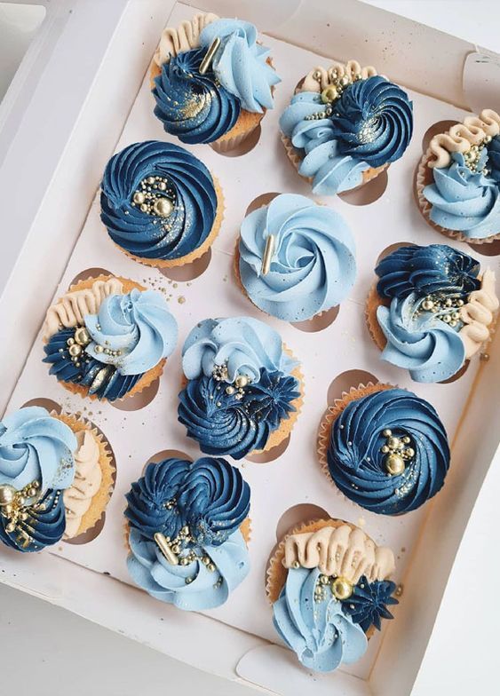 a box filled with blue cupcakes sitting on top of a white tablecloth