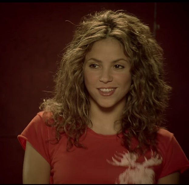 a woman with long curly hair is smiling for the camera while wearing a red shirt