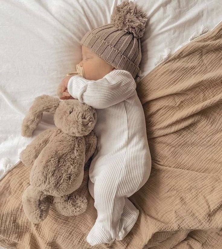 a baby sleeping with a stuffed animal on top of it's back in a bed