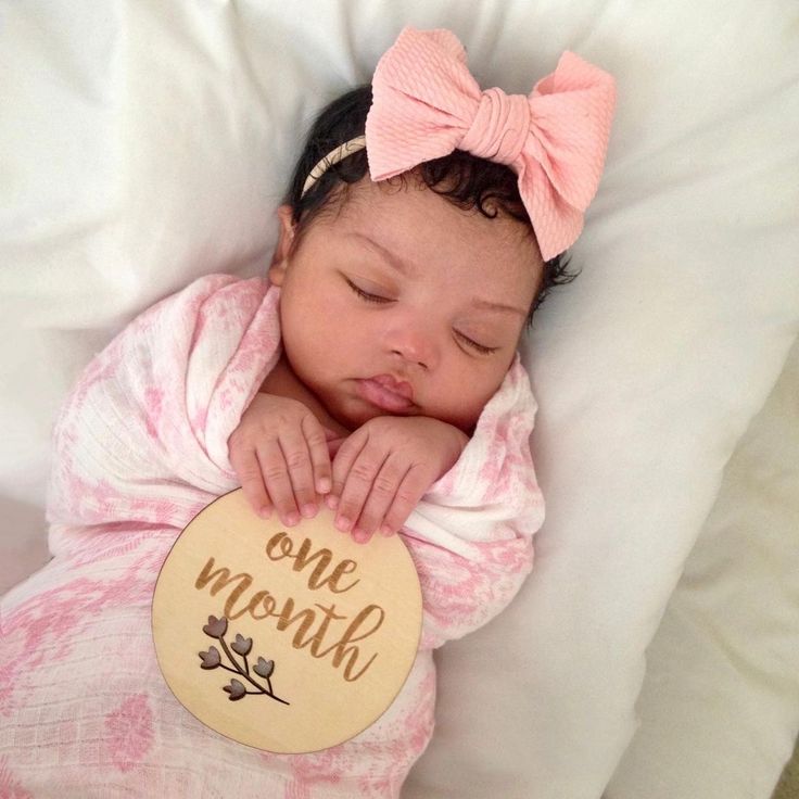 a baby girl is sleeping on her back with a wooden sign that says one month