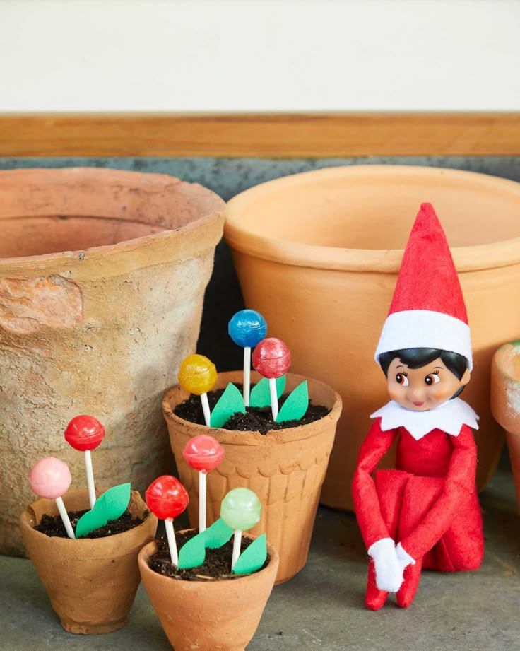 an elf sitting next to potted plants with candy lollipops on them