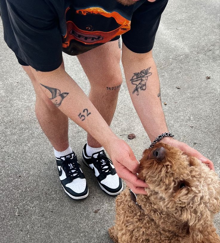 a man is petting a small dog on the street while wearing sneakers and holding it in his hand