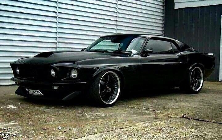 a black muscle car parked in front of a garage