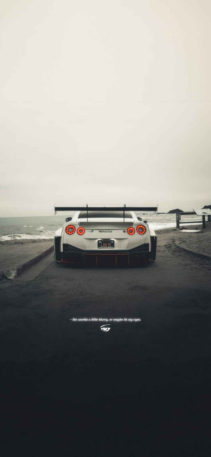 a white sports car parked on top of a parking lot next to the ocean in front of an overcast sky