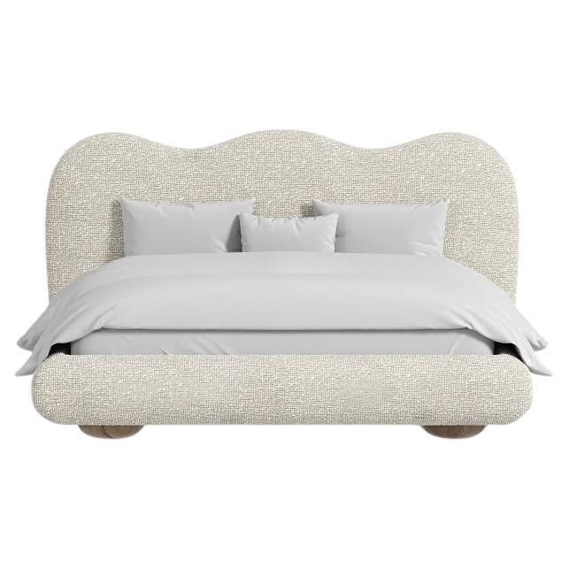 an upholstered bed with white linens and pillows on the headboard, in front of a white background