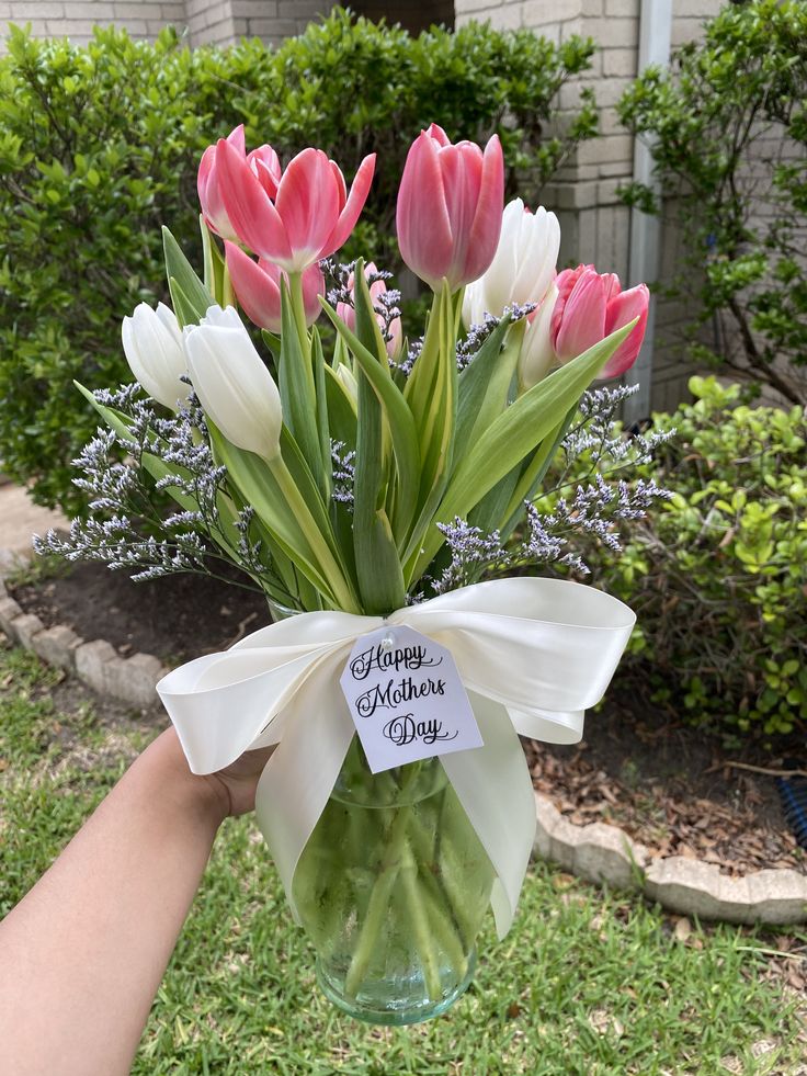 a vase filled with pink and white tulips sitting on top of a grass covered field