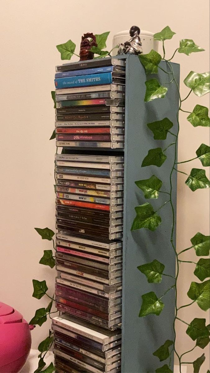 A collection of CDs in a rack covered by fake Ivy. Music Collection Aesthetic, Dvd Shelf Aesthetic, Cd Setup Aesthetic, Cd Shelf Aesthetic, Cd Storage Aesthetic, Cd Holder Aesthetic, Physical Media Aesthetic, Cd Shelf Ideas, Diy Cd Storage