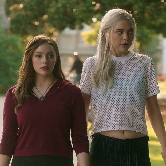 two young women walking down the street with their hands in their pockets and looking at something