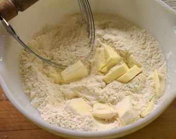 a bowl filled with flour and butter next to a whisk on top of a wooden table